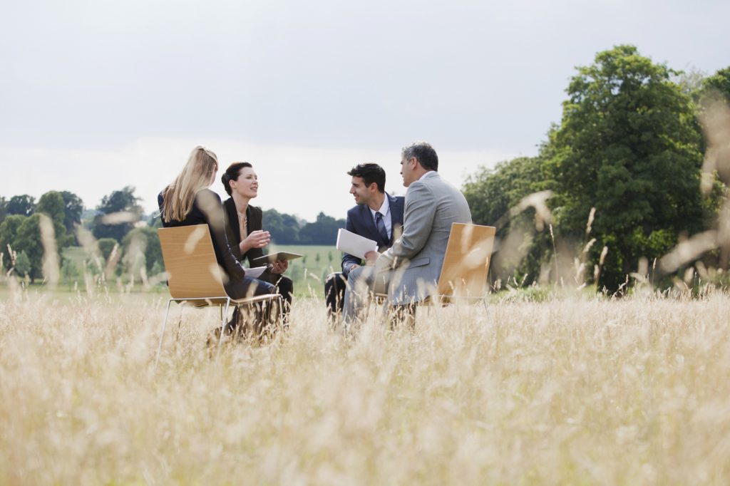 Vier Menschen sitzen auf Stühlen mitten auf einem Feld und diskutieren.